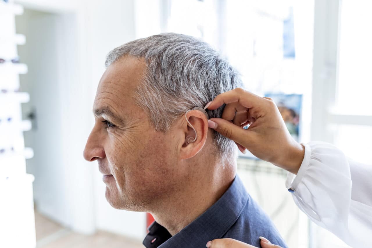 Photo of an audiologist inserting hearing aid in man's ear Photo of an audiologist inserting hearing aid in man's ear