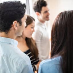 Young man with a hearing aid chatting with a group of friends.
