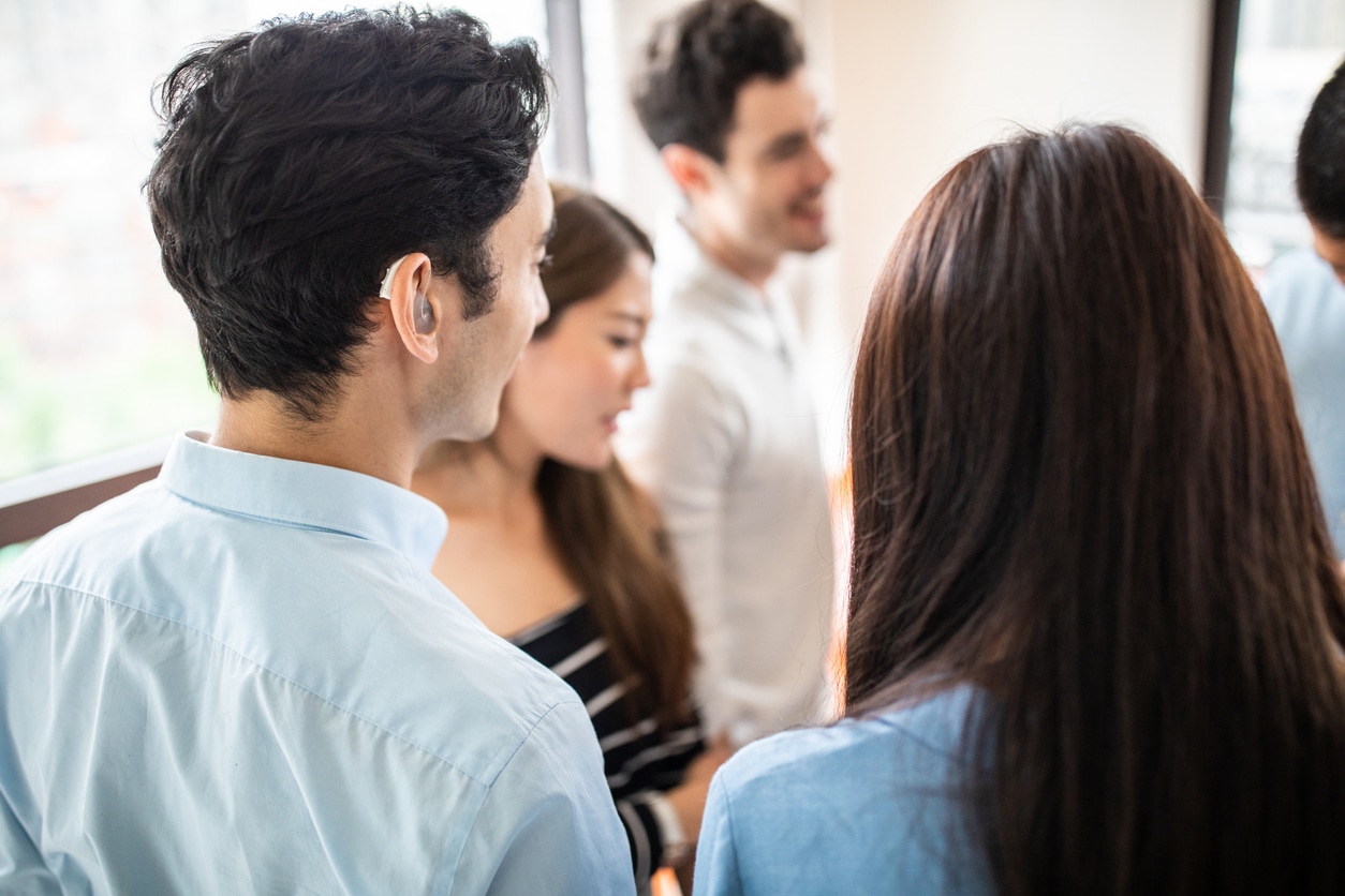 Young man with a hearing aid chatting with a group of friends.