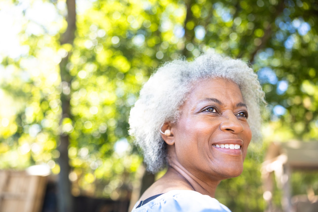 Senior woman smiling while showing off her hearing aid.
